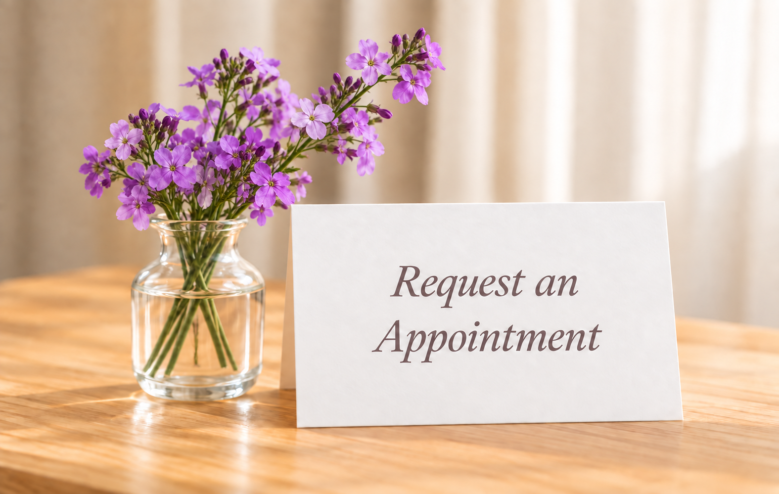 Light lavender flowers in a clear glass vase beside an Appointment Only card